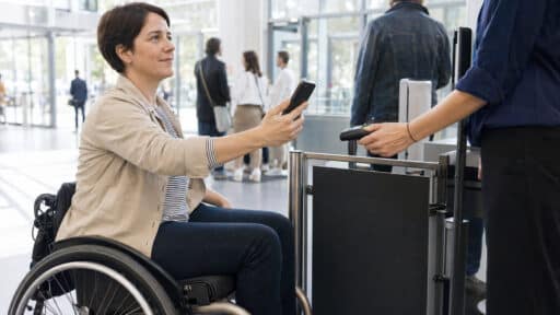 Eine Rollstuhlnutzerin hält am Eingang eines modernen Museums ihr Smartphone an ein digitales Prüfgerät.