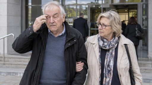 Mann mit schwerem Augenlidkrampf wird vor einem Gerichtsgebäude von seiner Ehefrau begleitet