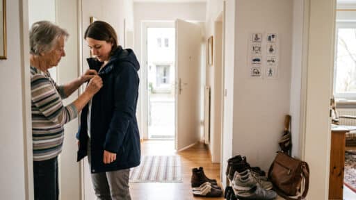 Eine Mutter hilft ihrer erwachsenen Tochter in einem Wohnungsflur ruhig beim Anziehen einer Jacke