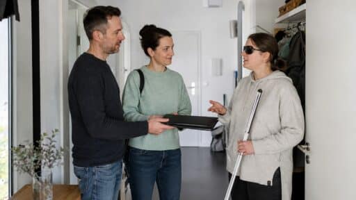 Blinde Frau bespricht in ihrer Wohnung den Schichtwechsel mit zwei persönlichen Assistenzkräften
