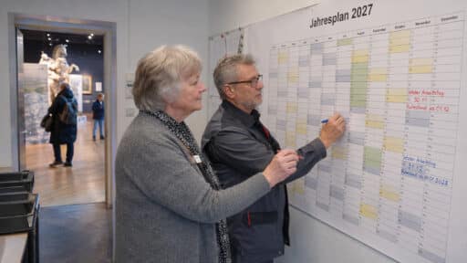 Zwei ältere Museumsmitarbeiter markieren ihre unterschiedlichen Rentenbeginne im Jahresplan 2027