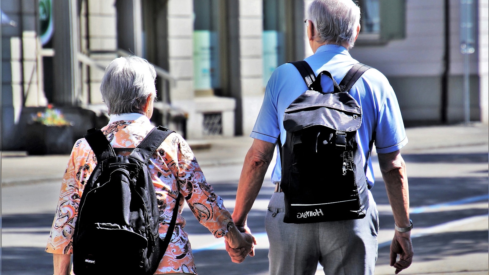 Hand in Hand geht ein Rentnerpaar eine lange Straße entlang, während Altersrenten im Schnitt fast 22 Jahre laufen.