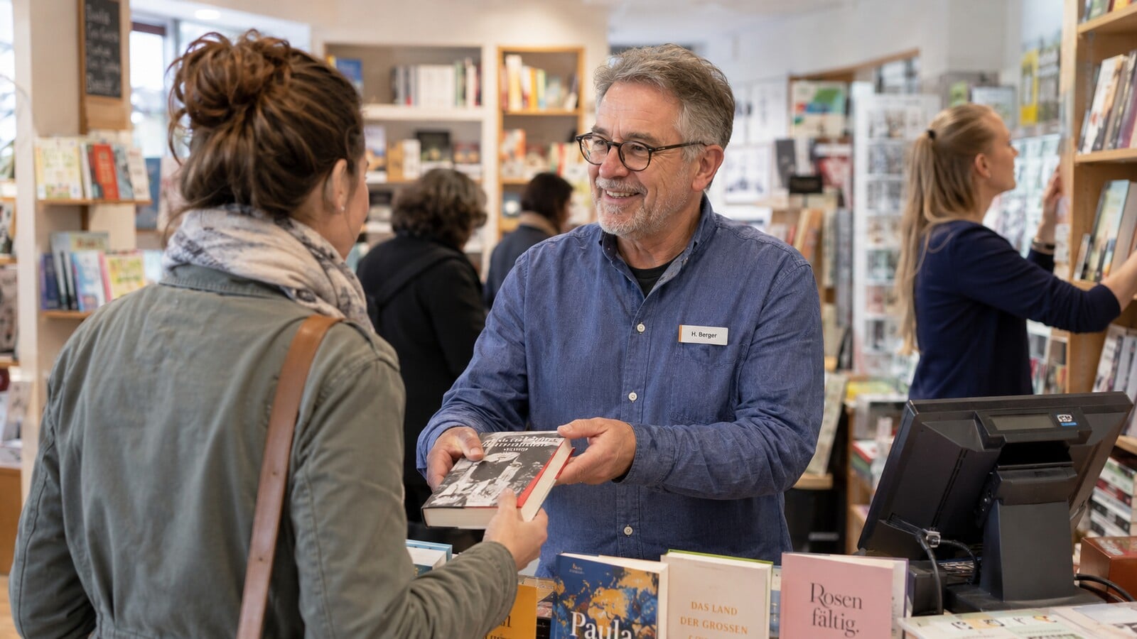 Älterer Mitarbeiter berät eine Kundin in einer Buchhandlung