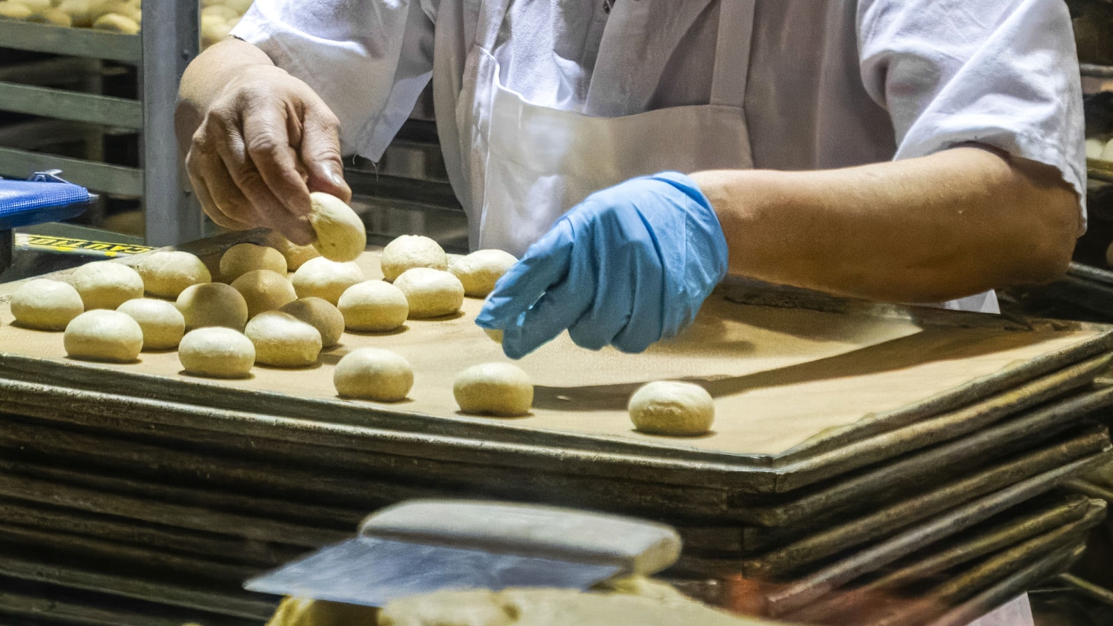 Hände formen in einer Produktionsbackstube Teiglinge und stehen für körperlich belastende Arbeit über viele Berufsjahre.