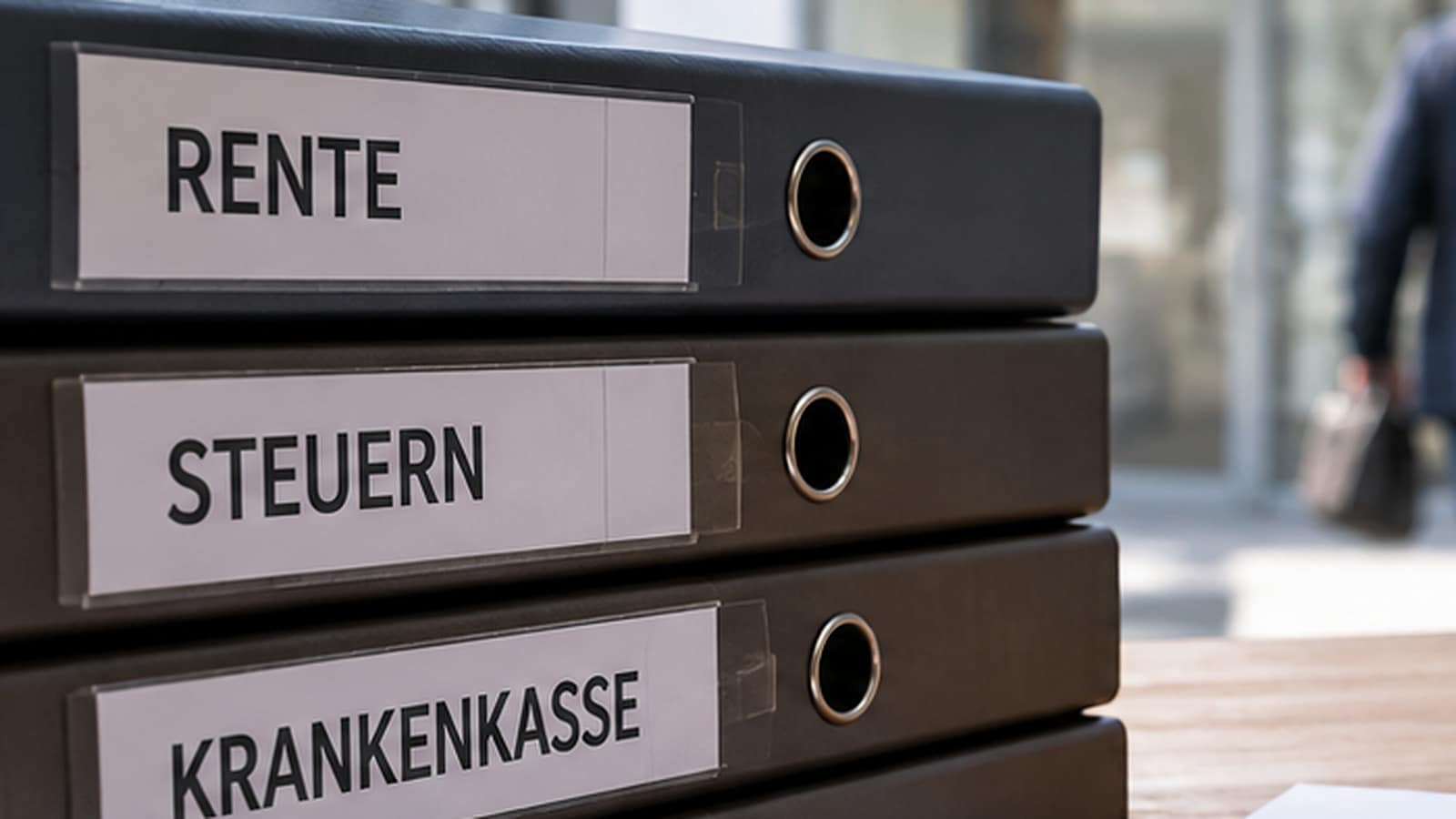 Aktenordner mit den Beschriftungen Rente und Steuern, im Hintergrund geht ein älterer Mann.